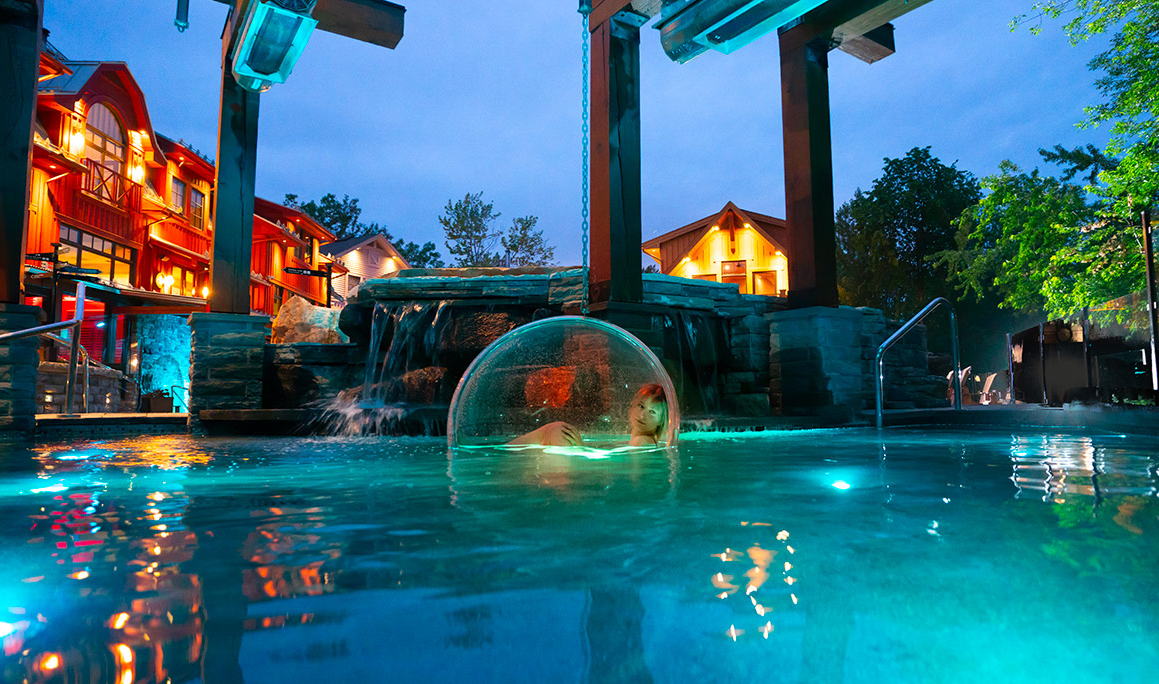 Femme assise dans une bulle de verre au centre de la piscine extérieure