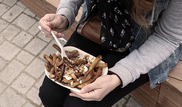 Person sitting on a bench eating poutine
