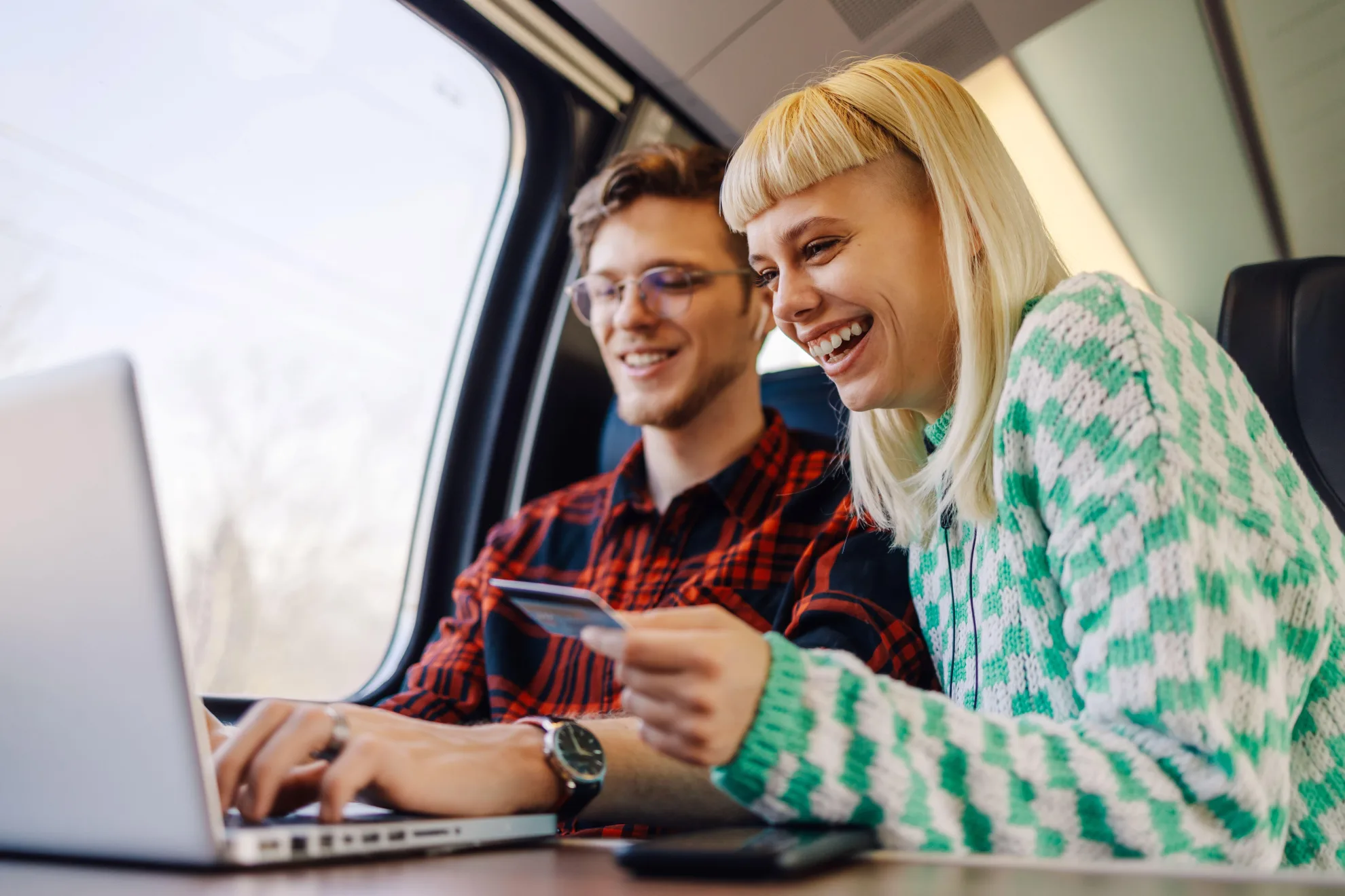 Deux voyageurs heureux assis dans un train devant un ordinateur portable